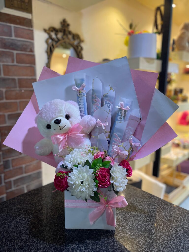 Sweet Hug Bloombox with teddy bear, chocolates, and artificial flowers in pink themed gift packaging